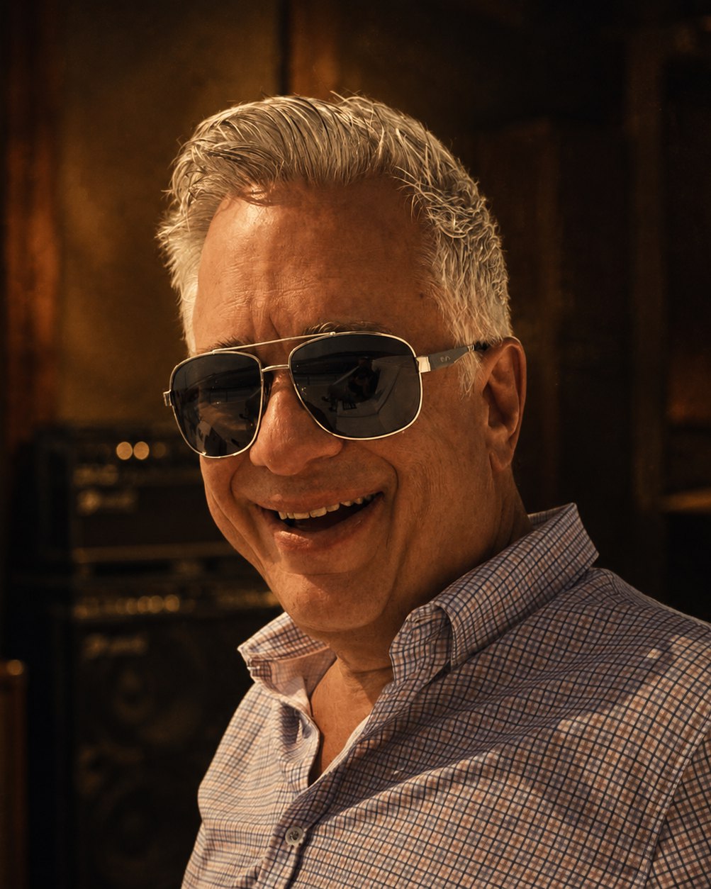 David Alan laughing, aviator sunglasses and silver hair, amplifiers stacked behind him.